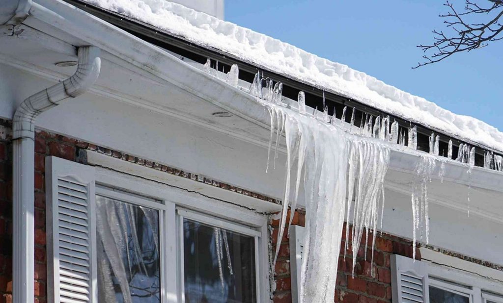 Heavy ice and icicles hanging from an eavestrough pulling away from the fascia board in winter