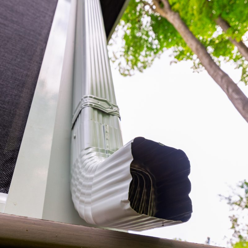 close up of curved end of downspout drainage system shown in white aluminum