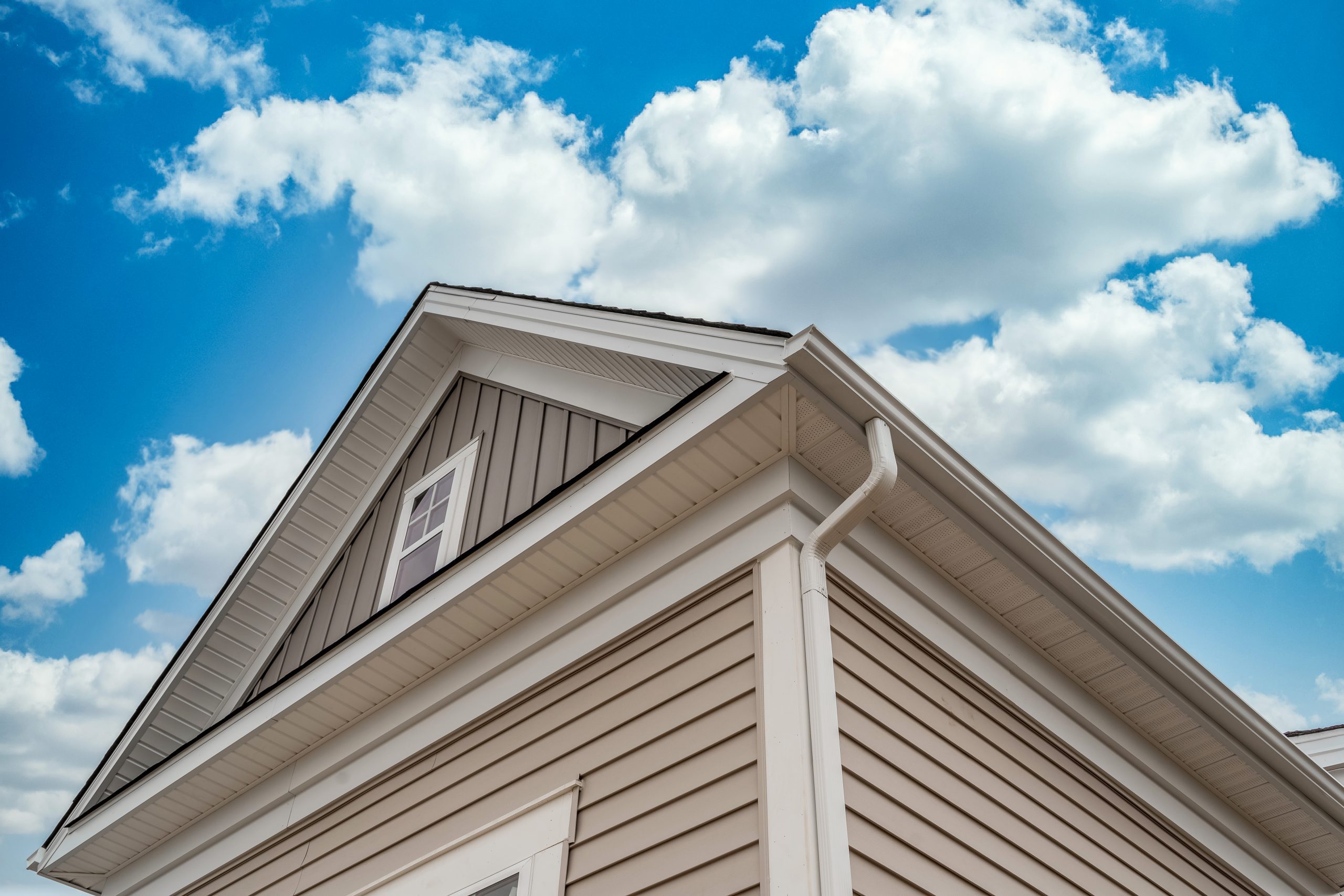 New soffit and fascia installation in white aluminum on beige sided house against blue sky with white clouds